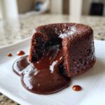 A rich, dark chocolate lava cake cut open, revealing molten chocolate flowing onto a white plate.
