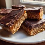 Several squares of rich graham cracker toffee with a crunchy base, caramel layer, and thick chocolate topping, served on a white plate.