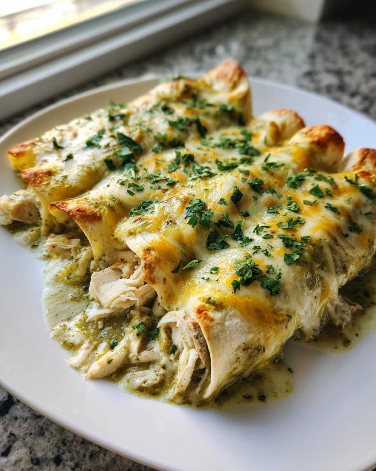 Three rolled green chile chicken enchiladas covered in melted cheese and fresh cilantro on a white plate.