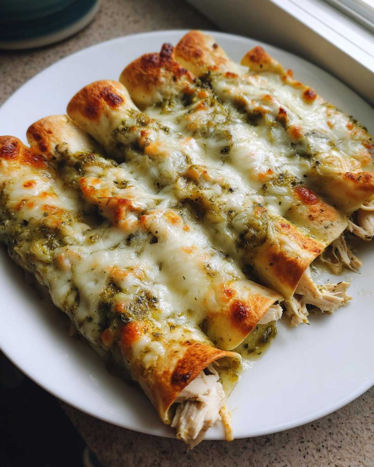 Four baked green chile chicken enchiladas covered in melted white cheese on a white plate.