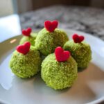 Five bright green Grinch Oreo balls coated in sprinkles, each topped with a small red candy heart.