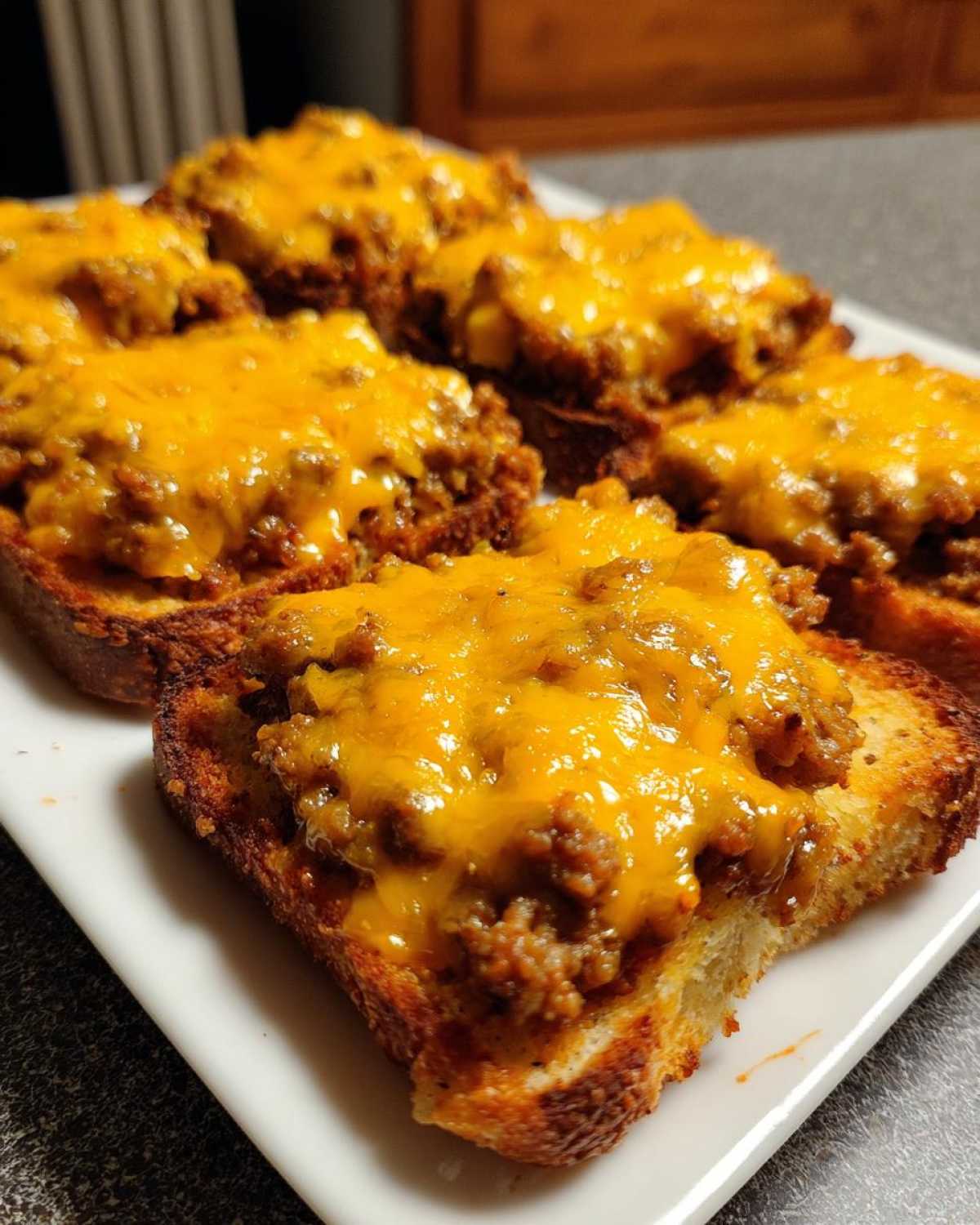 Close-up of several pieces of toasted bread topped with savory meat mixture and melted cheddar cheese, representing the hanky panky recipe.