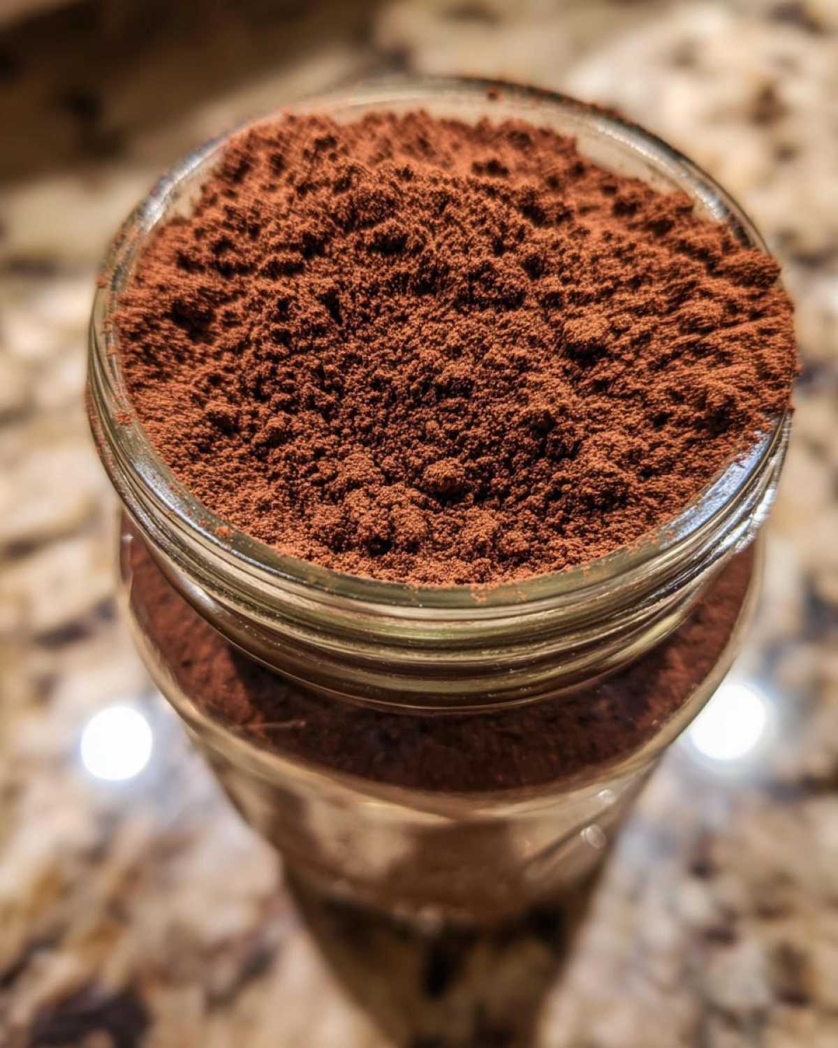 Overhead close-up view of rich brown hot cocoa mix powder filling the top of a clear glass jar.