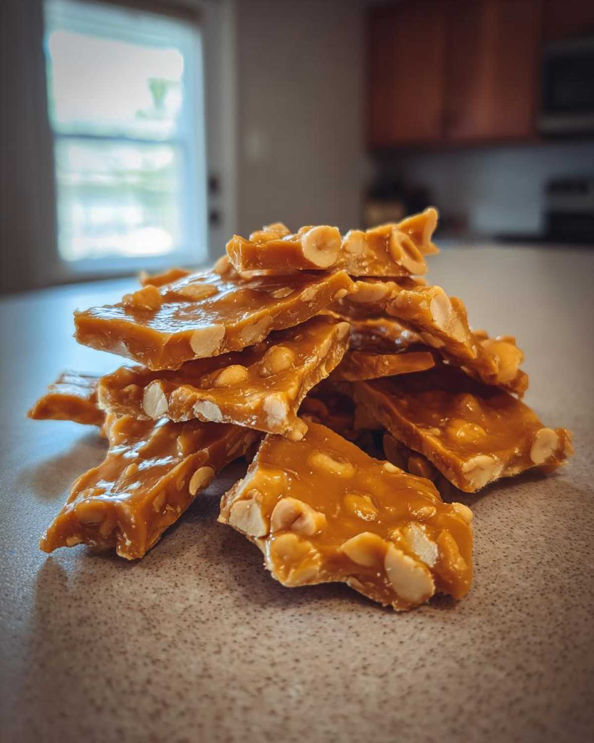A stack of freshly broken pieces of homemade peanut brittle recipe on a speckled countertop.