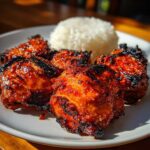 Four pieces of glistening, charred harissa chicken thighs served next to a mound of white rice on a white plate.