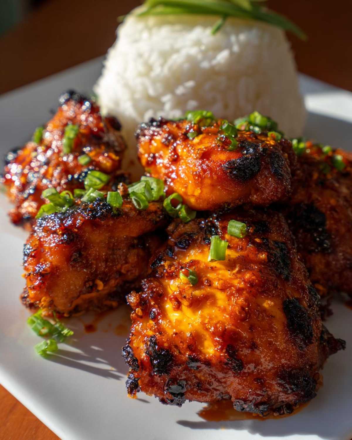 Close-up of glazed, slightly charred harissa chicken pieces served next to a mound of white rice, garnished with green onions.