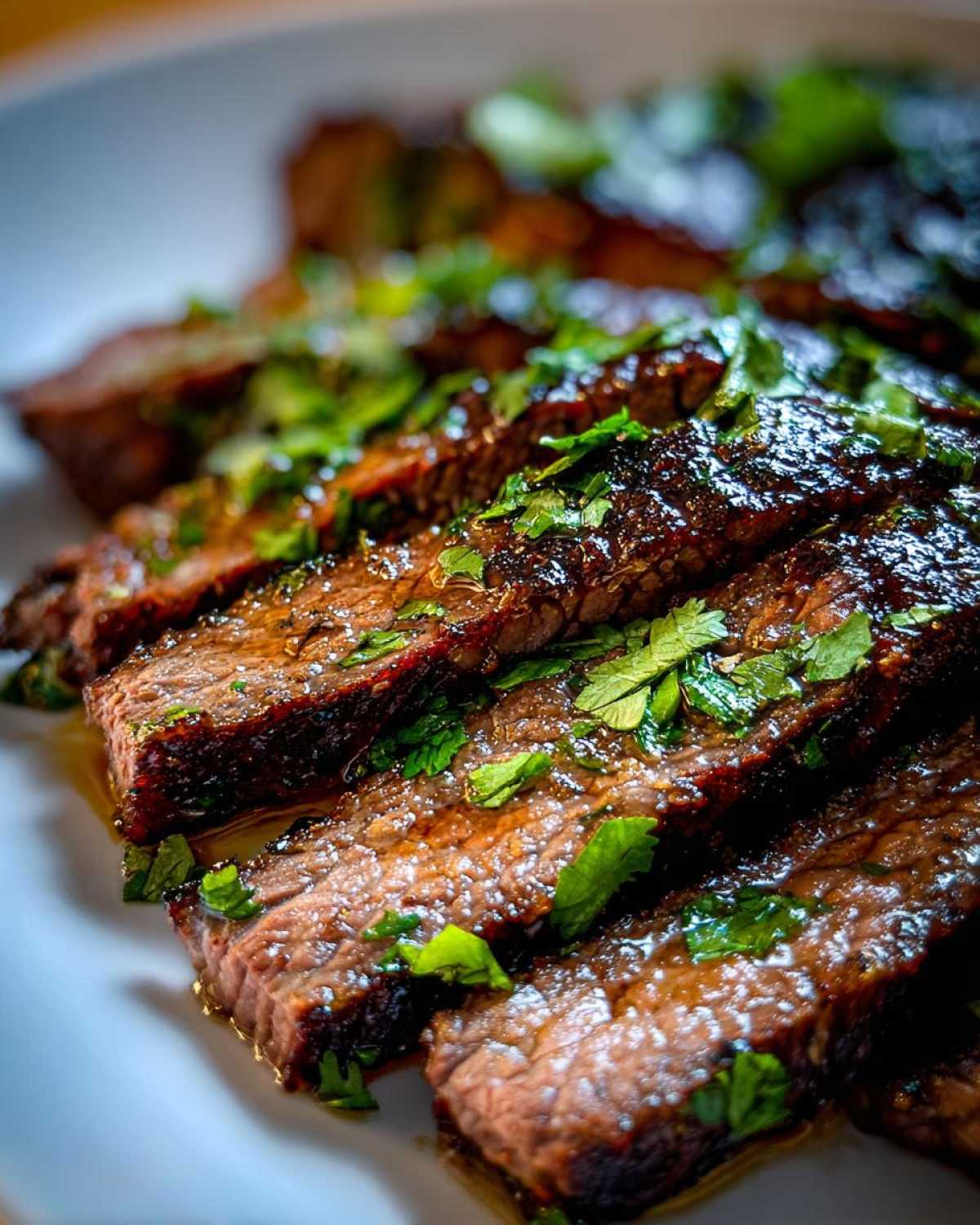 Close-up of perfectly cooked, sliced steak glistening with a rich Carne asada marinade and topped with fresh cilantro.