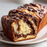 Close-up of a freshly baked chocolate babka loaf, showing the rich chocolate swirl interior and chocolate drizzle topping.