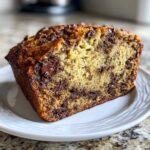 Close-up of a thick slice of moist chocolate chip banana bread on a white plate.