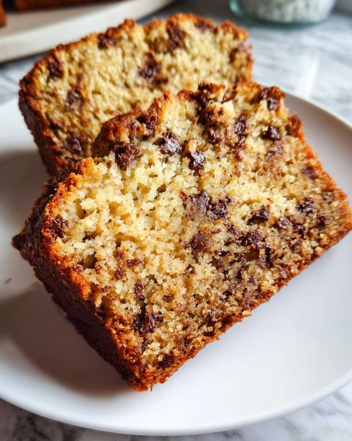 Close-up of two moist slices of chocolate chip best banana bread served on a white plate.