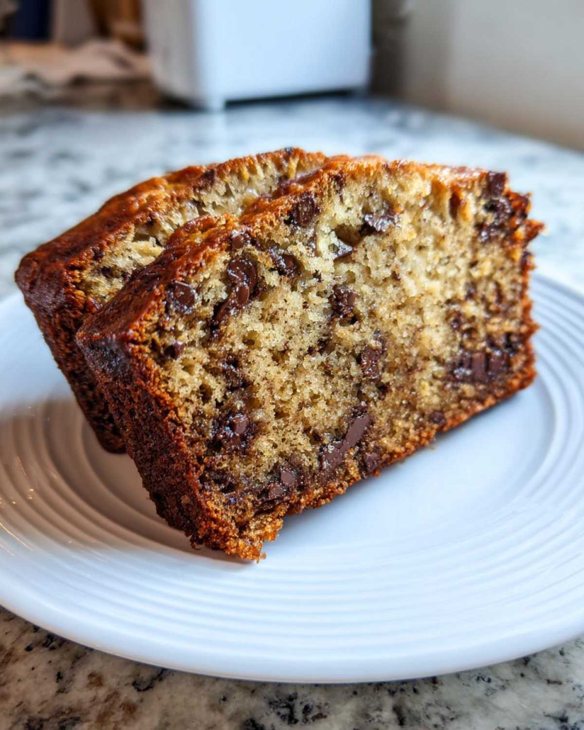 Two thick slices of moist chocolate chip best banana bread resting on a white plate.
