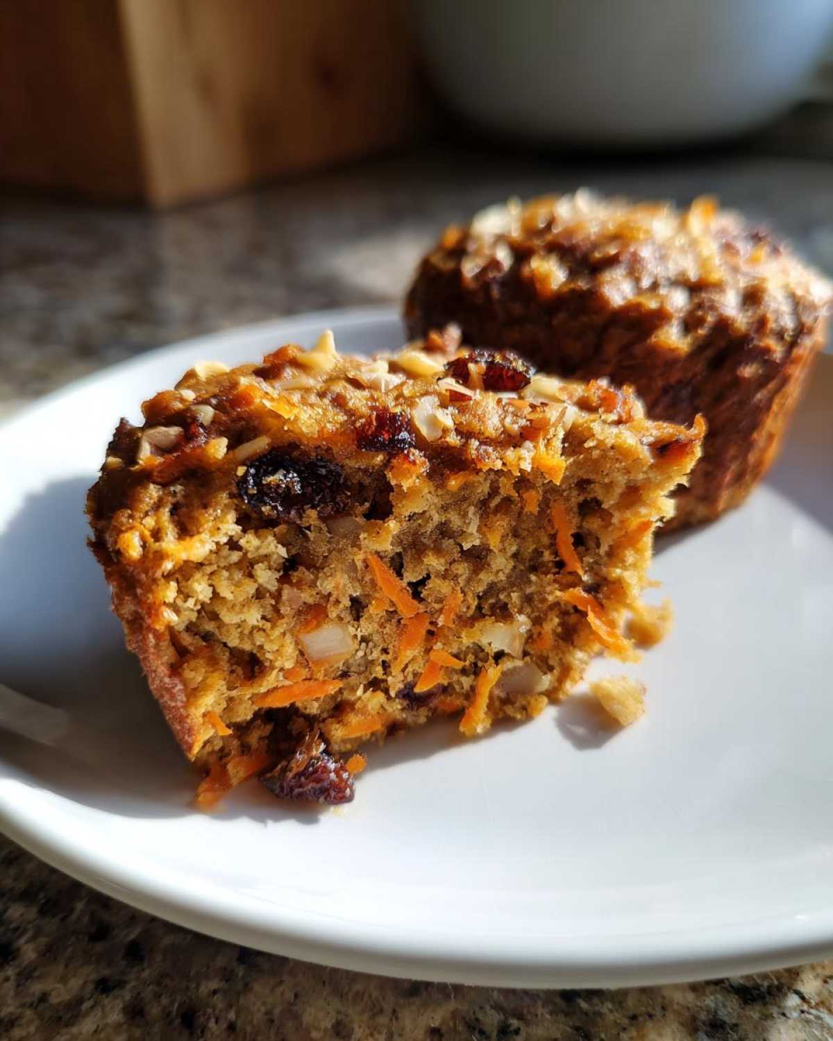 Close-up of a morning glory muffin cut in half showing moist texture, shredded carrots, raisins, and nuts.