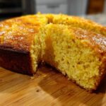 Close-up of a golden, moist slice cut from a round skillet cornbread on a wooden board.