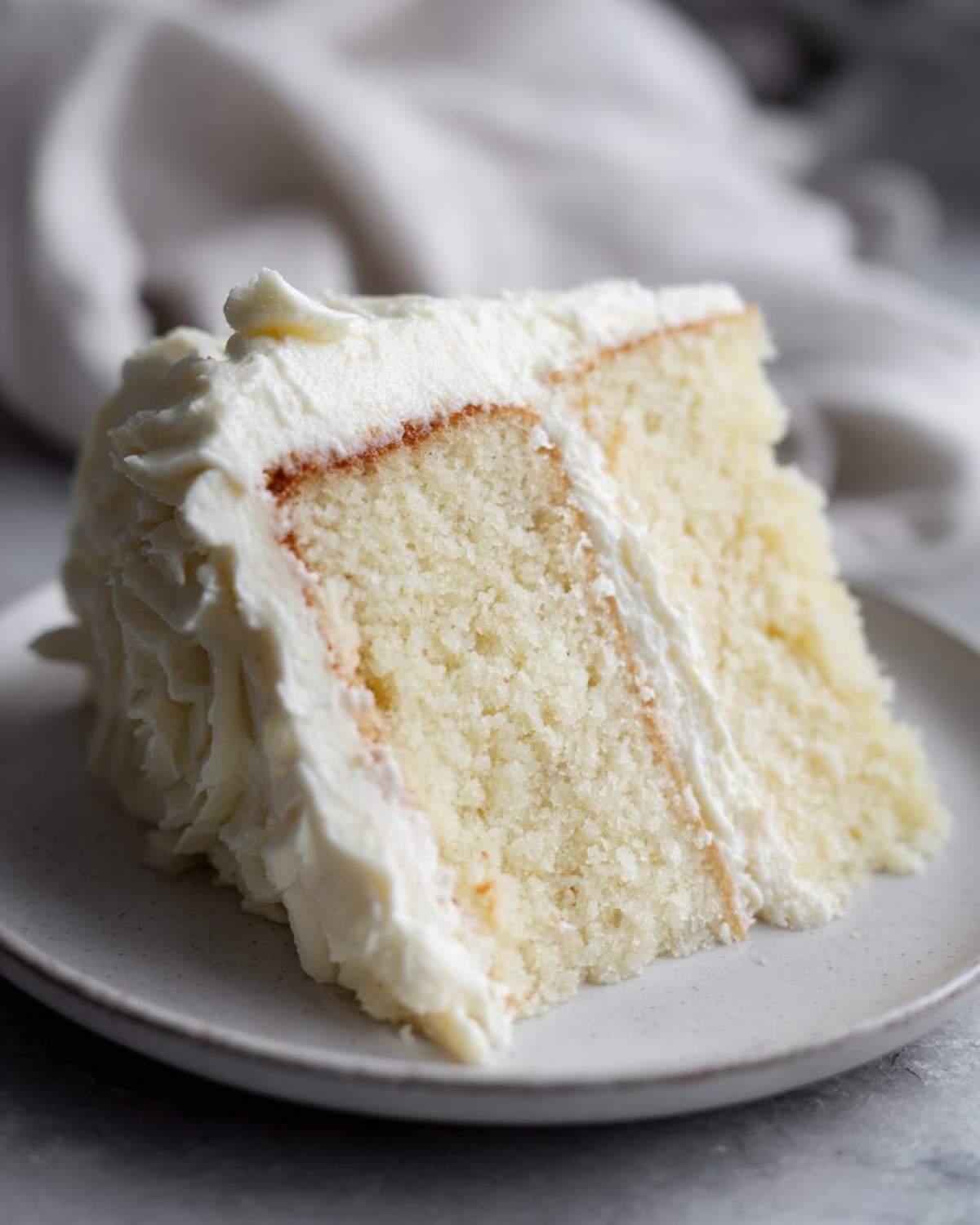 Close-up of a moist slice from the best vanilla cake recipe, layered with white frosting.