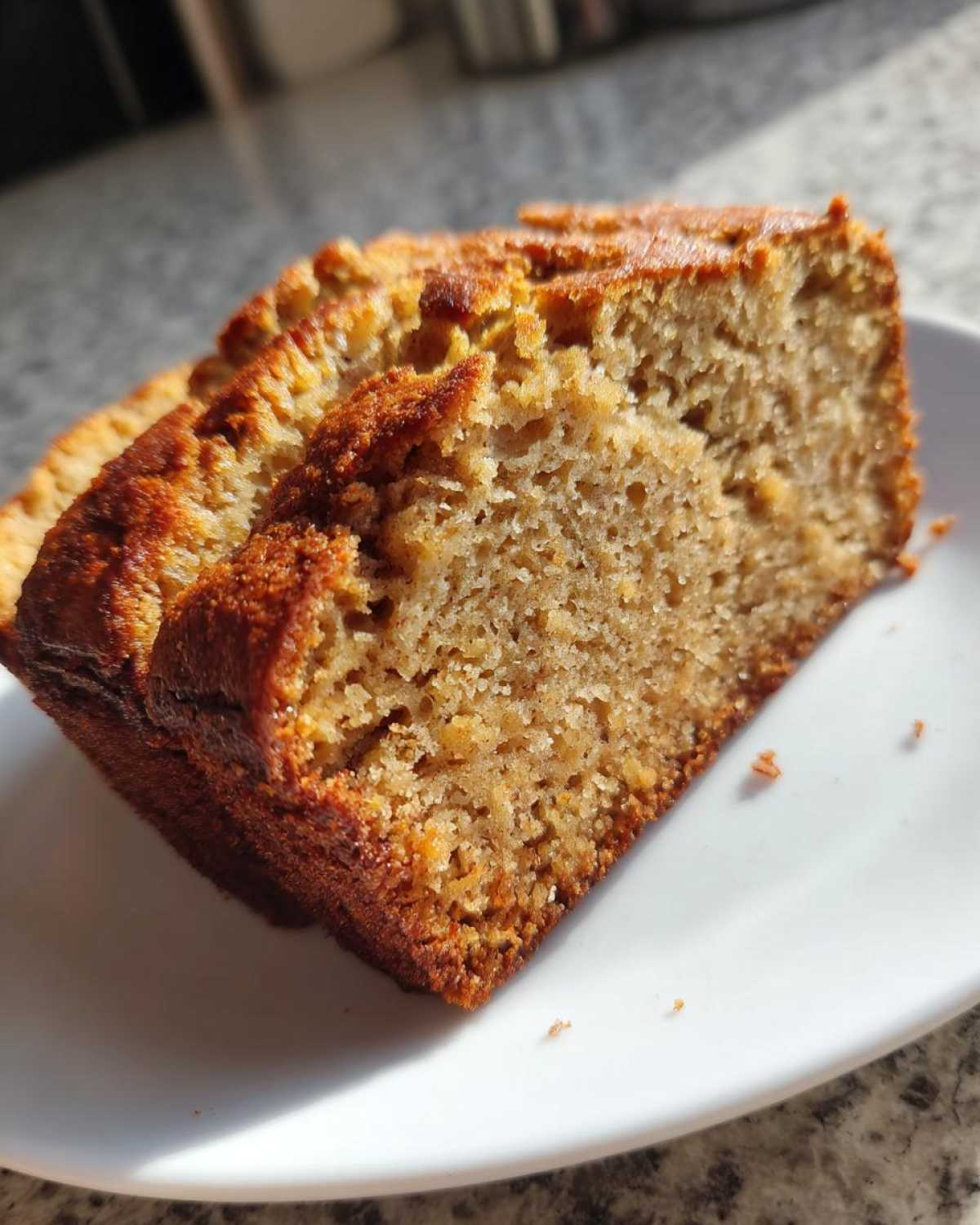 Close-up of two moist slices of golden brown sugar free banana bread served on a white plate.