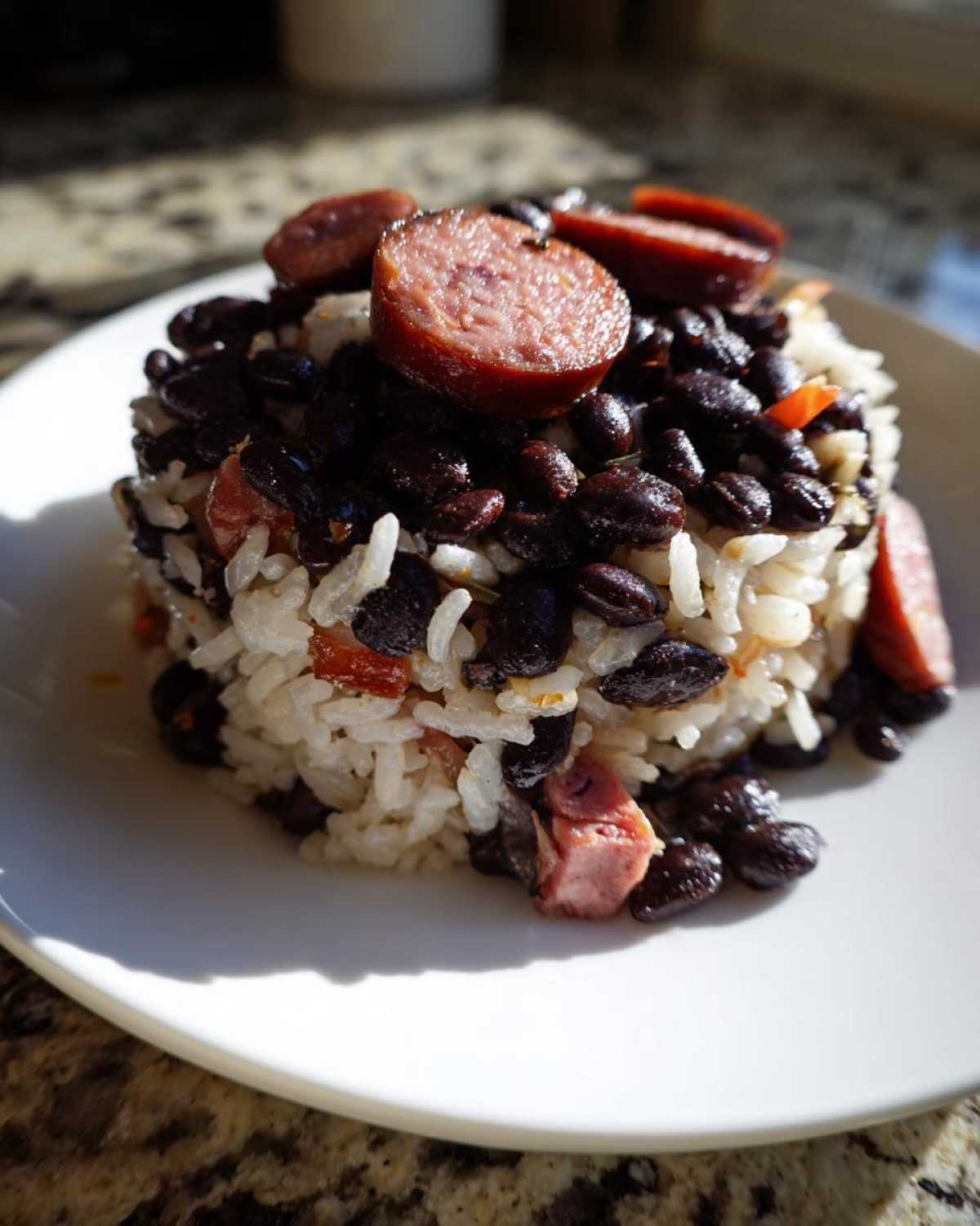 A molded serving of white rice mixed with dark black beans and topped with slices of smoked sausage, representing black beans and rice.