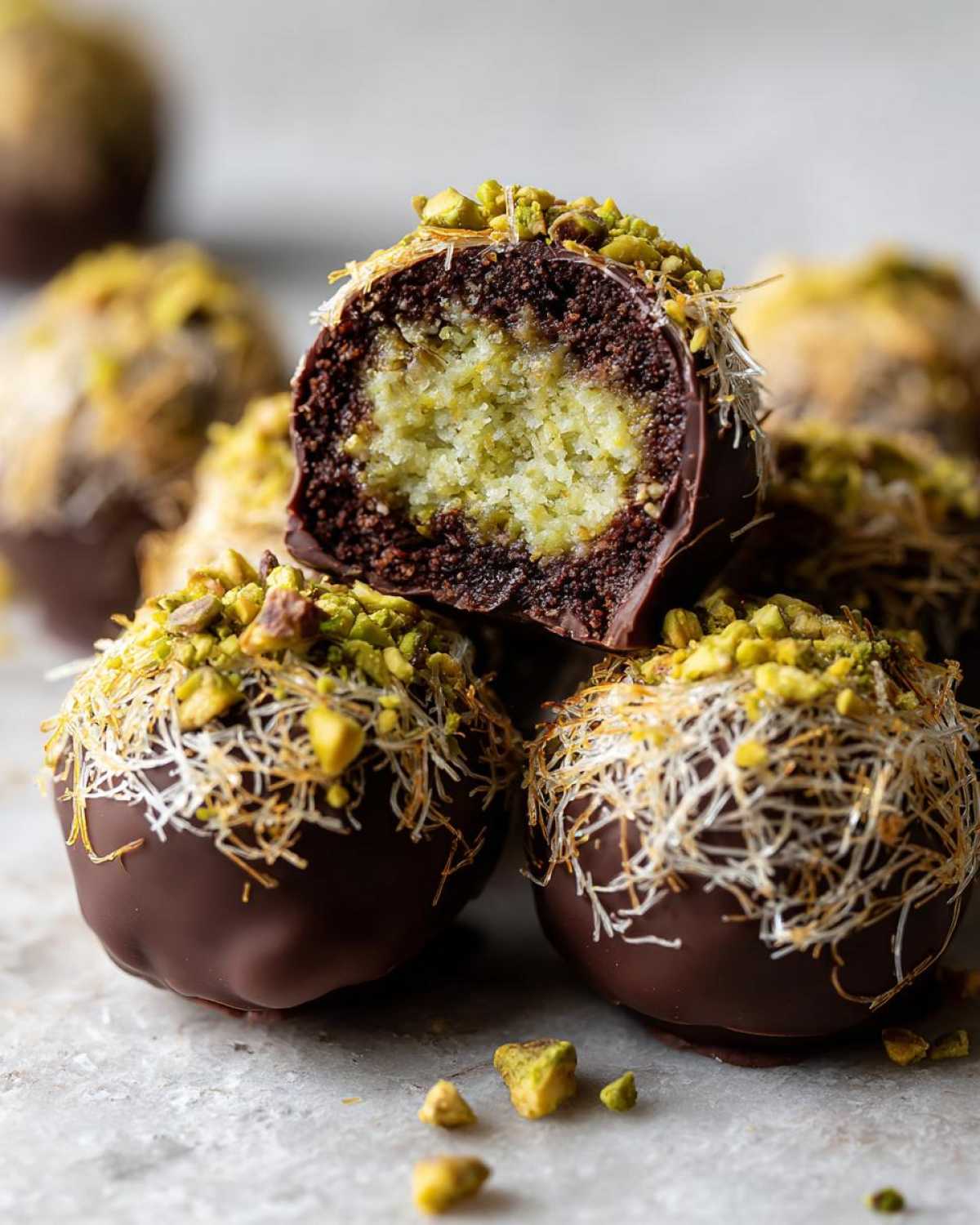 Close-up of a halved dubai chocolate balls showing a green pistachio center, coated in dark chocolate and shredded pastry.