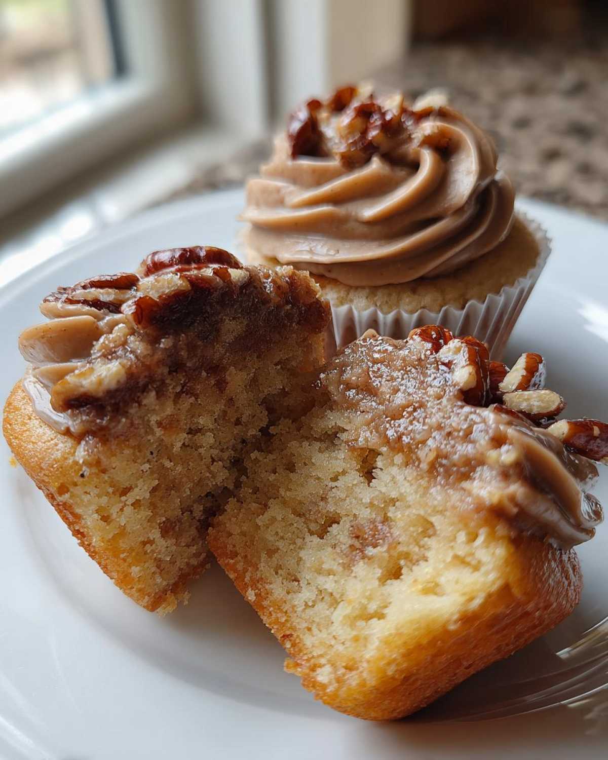 Close-up of pecan pie cupcakes, one cut in half showing the moist interior and pecan topping.