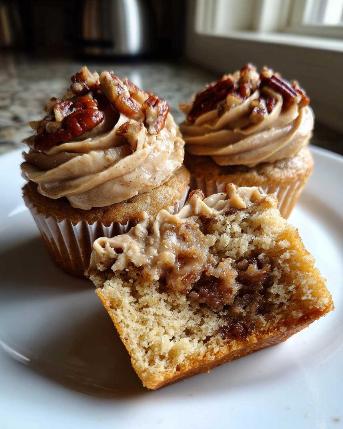 Three pecan pie cupcakes on a white plate, one cut open showing the gooey pecan filling inside the cake.