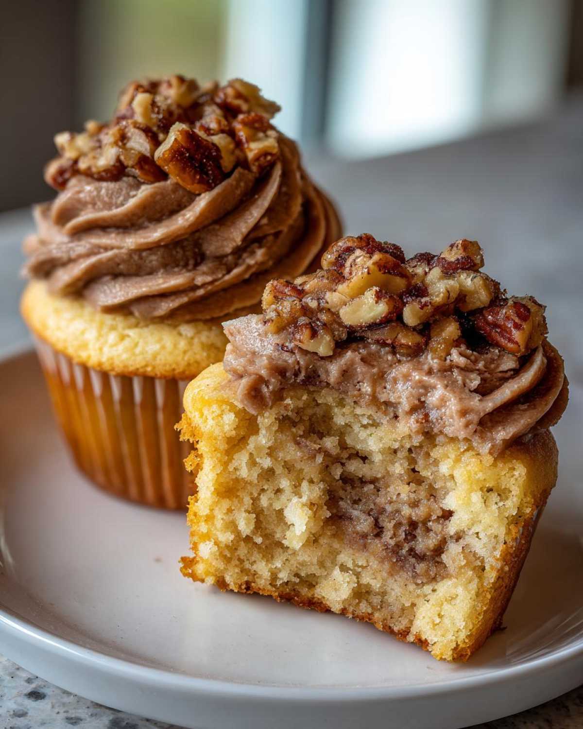 Close-up of a pecan pie cupcake cut in half showing the filling, with another whole pecan pie cupcake behind it.