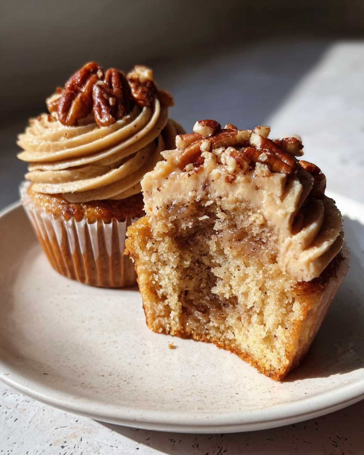 Close-up of a pecan pie cupcake cut in half showing the moist interior, topped with pecan frosting and pecans.