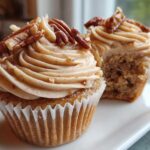 Two delicious pecan pie cupcakes, one whole and one bitten, topped with pecan pieces and brown sugar frosting.