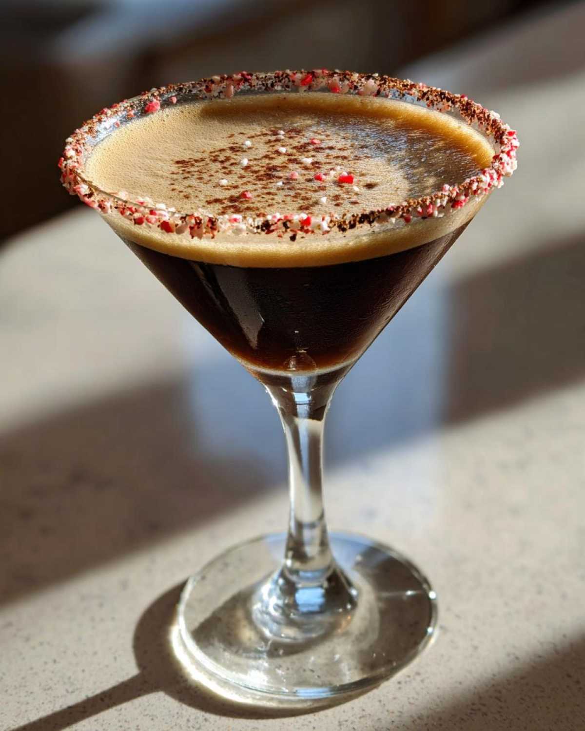 A rich peppermint espresso martini in a coupe glass, featuring a candy cane rim and cocoa dusting.
