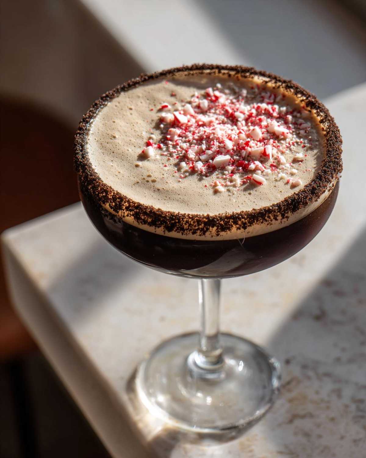 A rich peppermint espresso martini in a coupe glass, topped with foam and crushed candy canes.