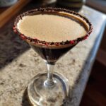 A rich peppermint espresso martini in a martini glass with a chocolate and crushed candy cane rim.