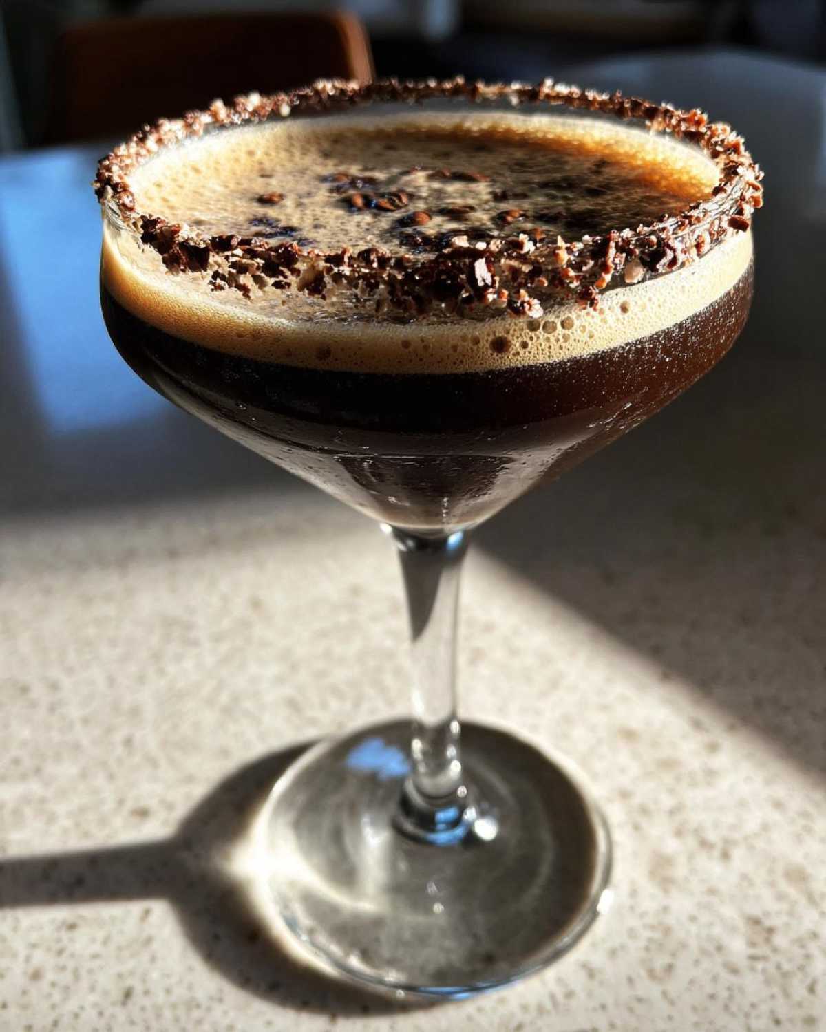 A dark peppermint espresso martini in a coupe glass with a thick chocolate rim and foam topping.