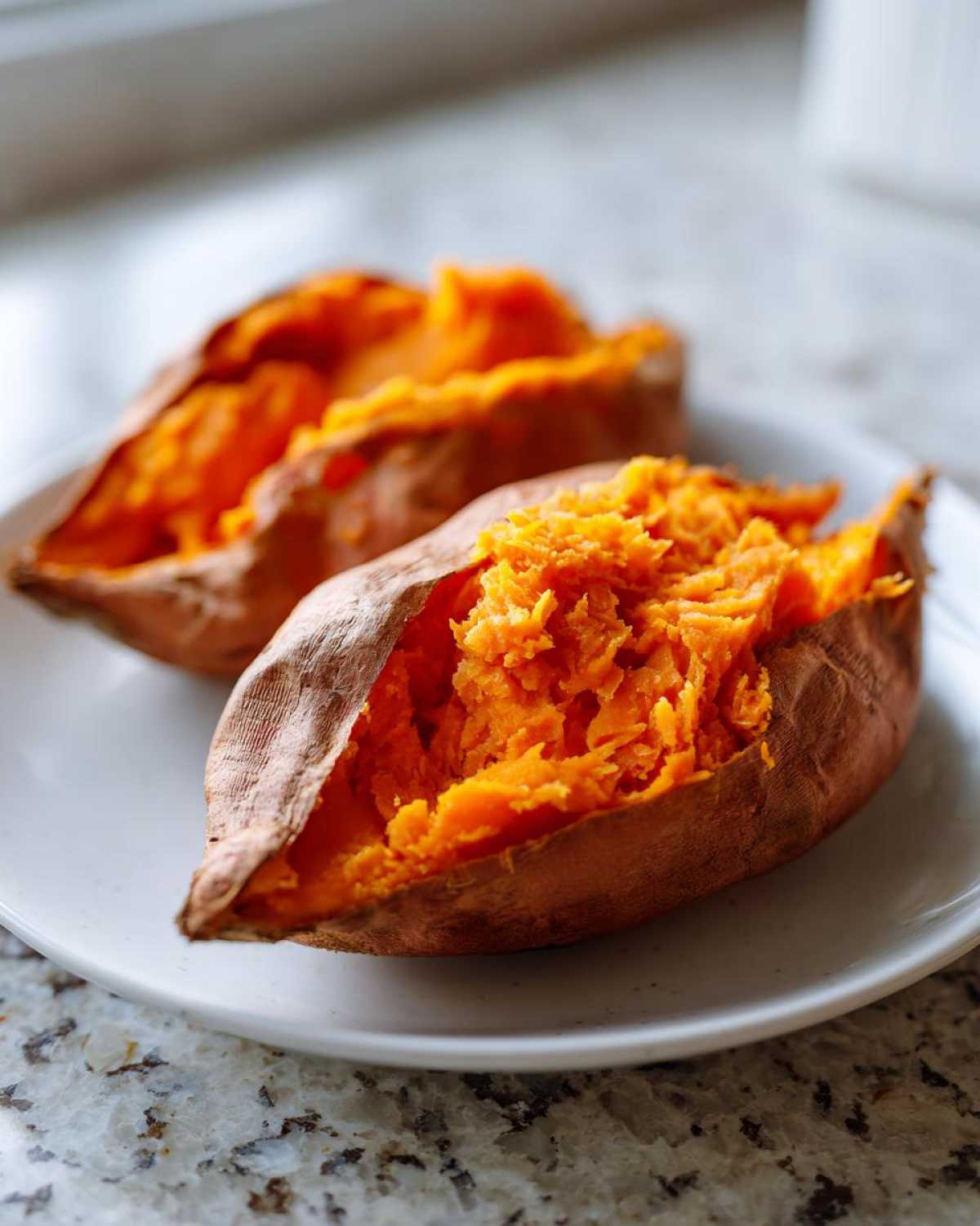 Two halves of a perfectly cooked baked sweet potato showing fluffy, bright orange flesh.