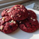 A stack of five vibrant red velvet cake mix cookies studded with white chocolate chips, resting on a white plate.
