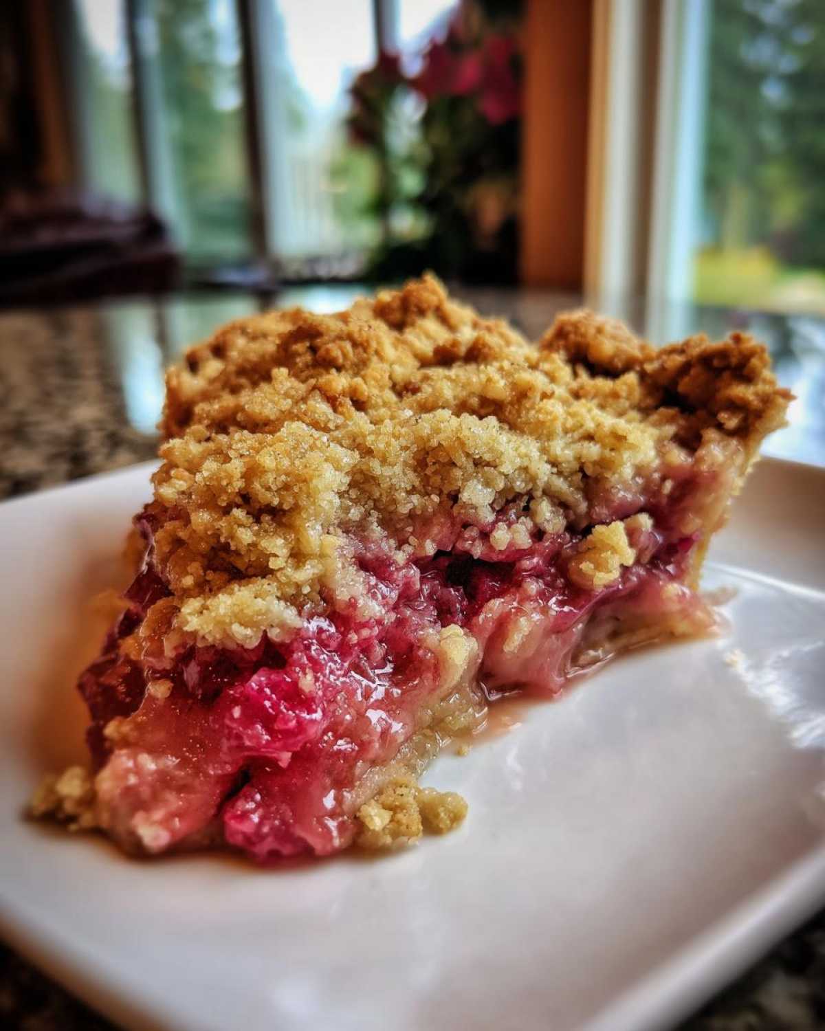 Close-up of a juicy slice of rhubarb crisp showing a thick, crumbly topping served on a white plate.