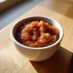 Close-up of chunky, spiced homemade applesauce served in a small white bowl on a wooden surface.