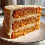 A tall slice of layered Creamsicle Cake with orange-tinted sponge layers and thick white frosting.