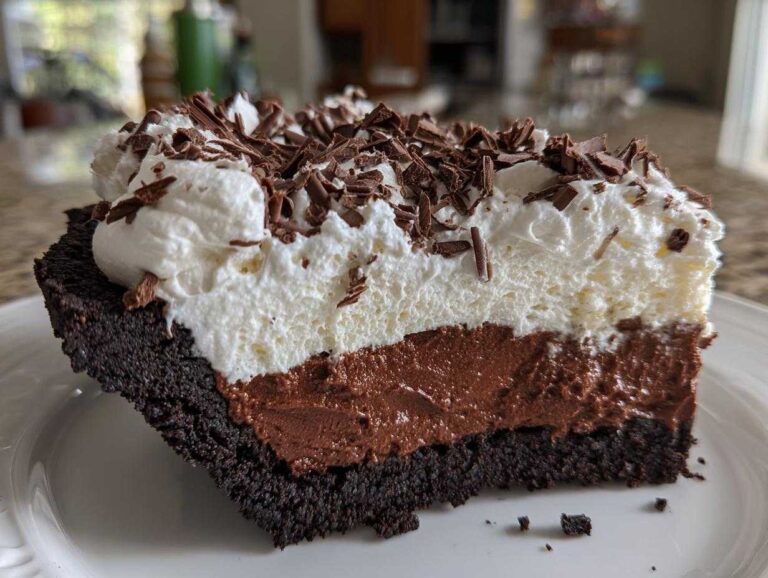 A thick slice of layered mud pie showing a dark crust, chocolate mousse filling, whipped cream, and chocolate shavings.