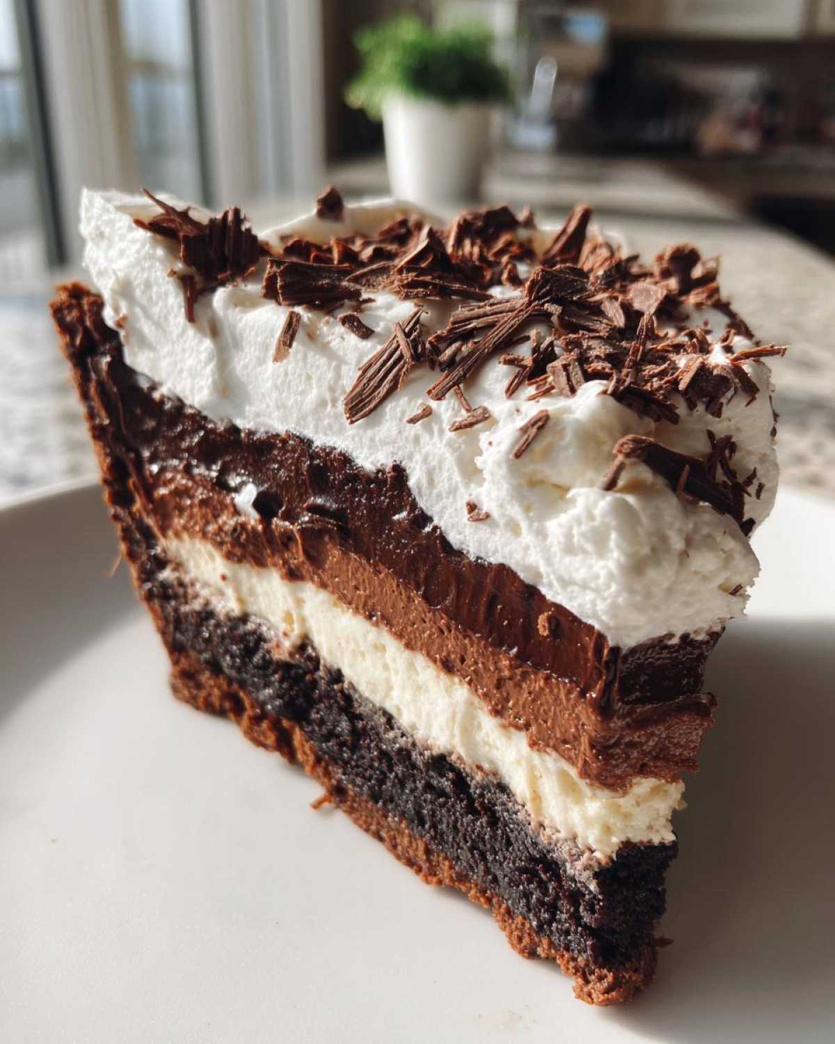 A decadent slice of multi-layered mud pie featuring a dark crust, cream layer, chocolate mousse, and whipped topping with chocolate shavings.