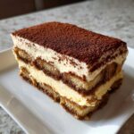 A thick, layered slice of homemade tiramisu recipe dusted heavily with cocoa powder.