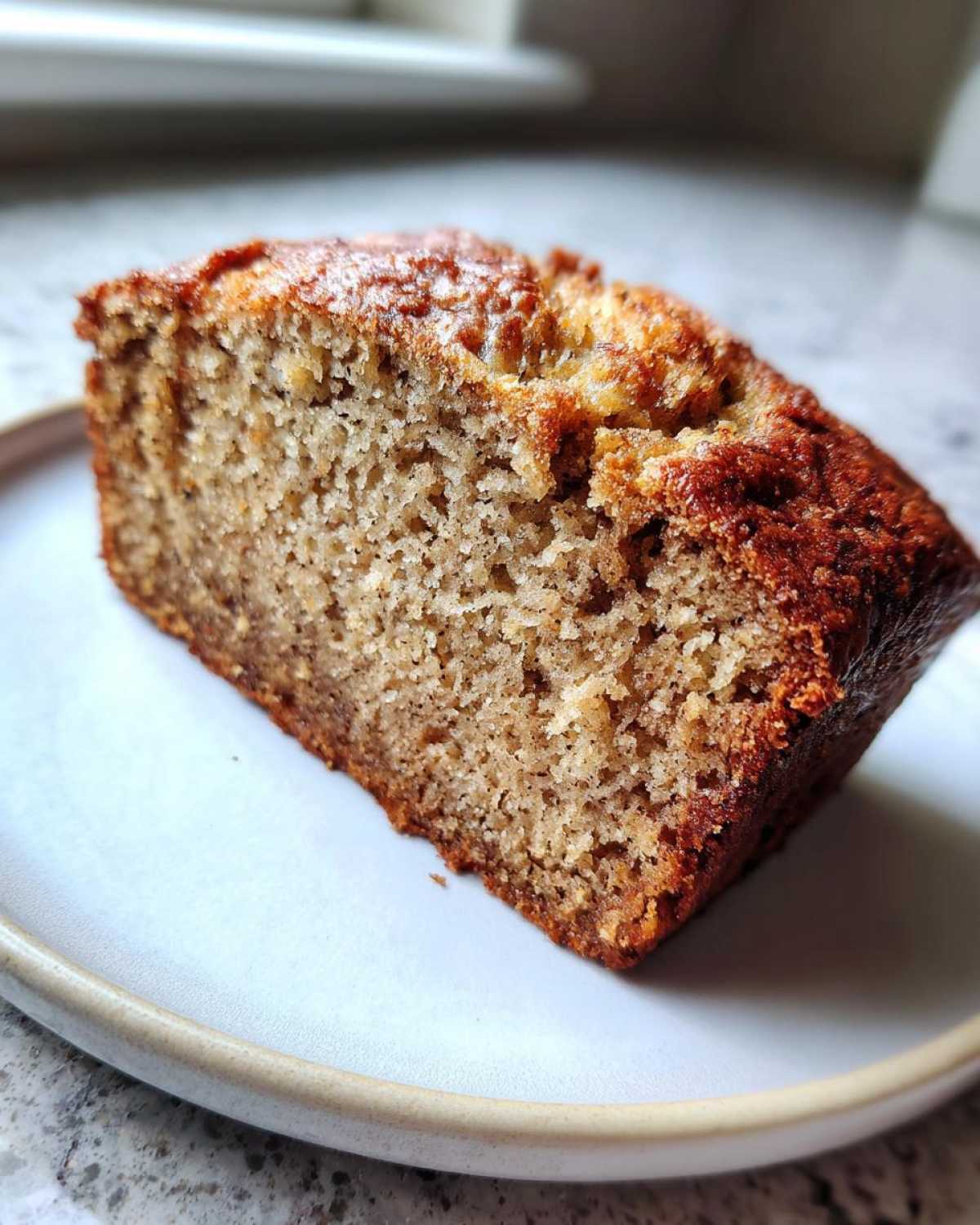 Close-up of a thick slice of moist sugar free banana bread on a light plate.