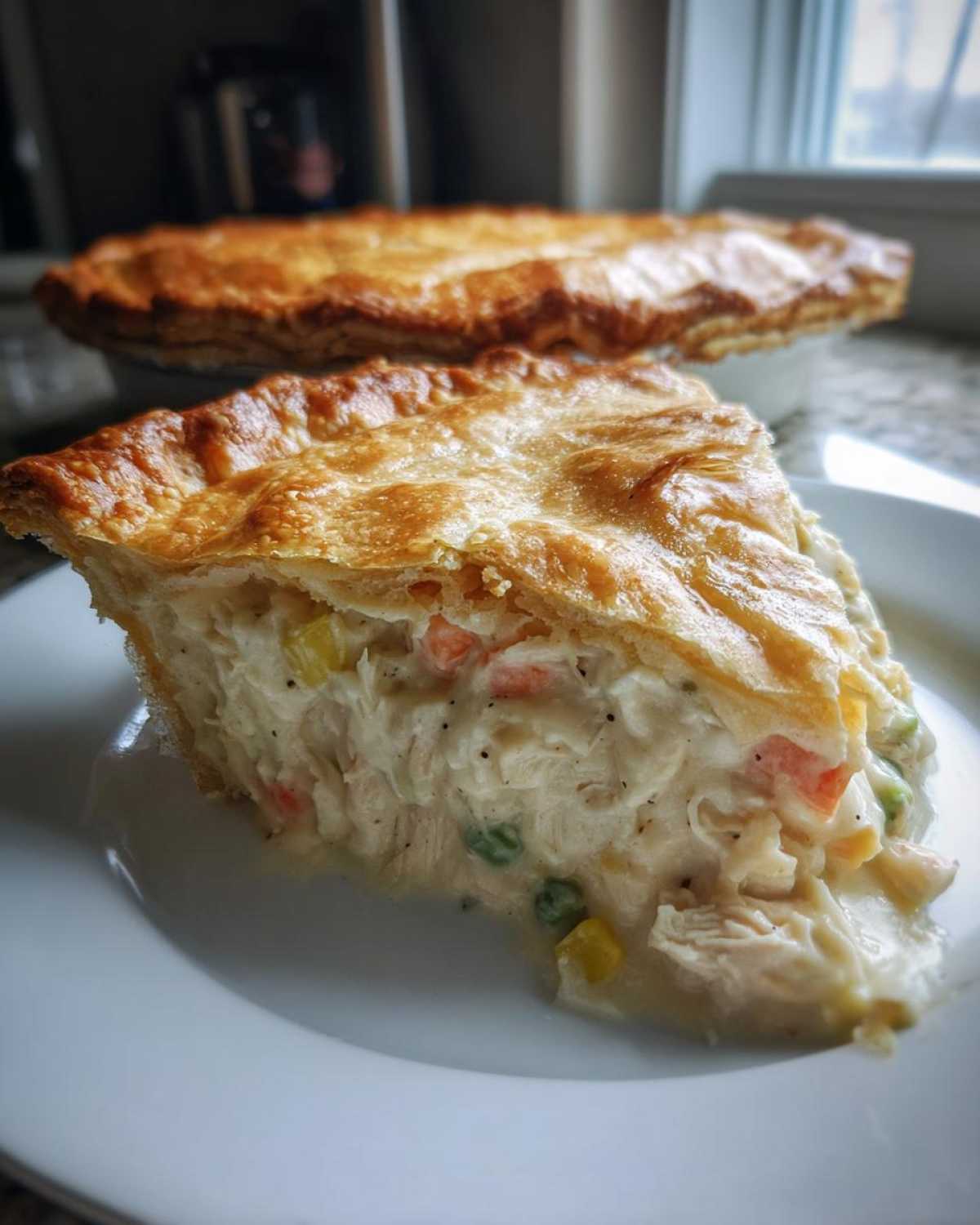 A thick slice of creamy turkey pot pie recipe showing shredded turkey, peas, carrots, and a golden flaky crust.