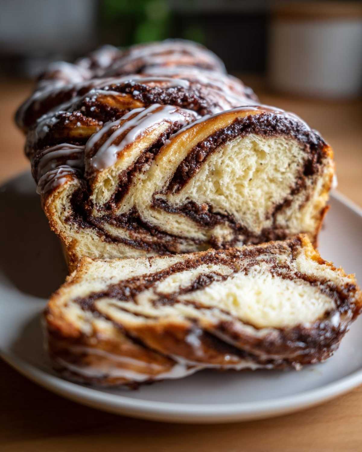 A close-up of a freshly baked chocolate babka, sliced to show the rich chocolate swirls and topped with a white glaze.