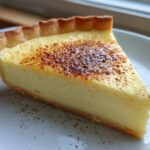 A perfect slice of smooth egg custard tart with a golden, lightly torched top, resting on a white plate.