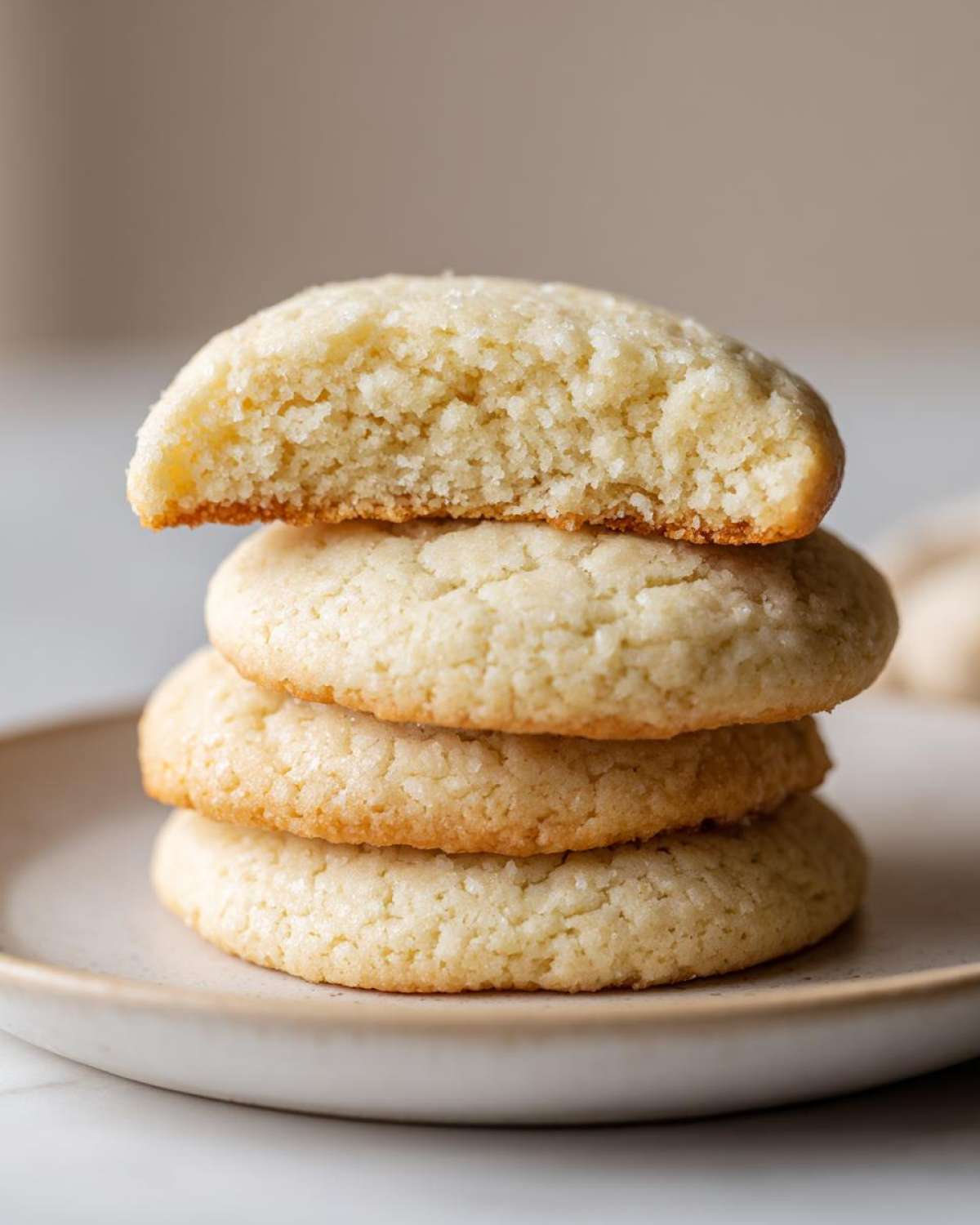 A stack of three soft sugar cookies, with the top one broken in half to show the fluffy interior texture.