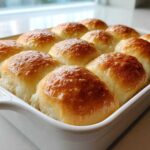 Twelve golden brown sourdough discard rolls baked together in a white ceramic dish.
