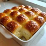 A pan of golden brown, glossy sourdough discard rolls, with one roll pulled away showing the soft interior.