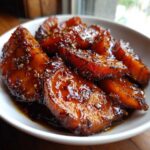 Thick slices of rich, dark glazed southern candied yams piled in a white bowl.
