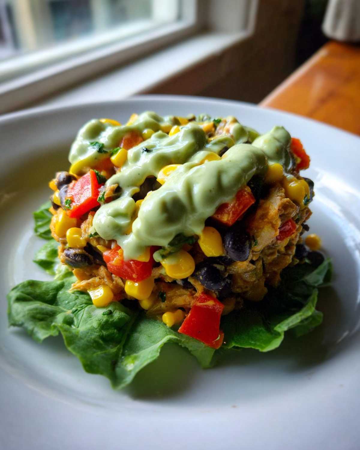 A molded portion of southwest chicken salad featuring corn, black beans, and red peppers, topped with a creamy green dressing, served on lettuce.