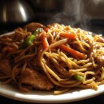 Close-up of hot, steaming chicken chow mein recipe with noodles, chicken pieces, carrots, and green peppers on a white plate.