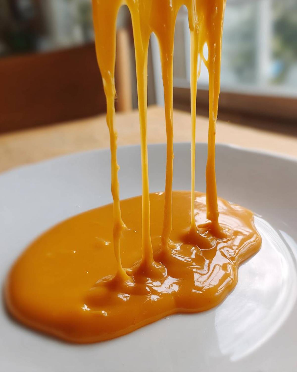 Close-up of thick, bright orange nacho cheese sauce dripping and stretching onto a white plate.
