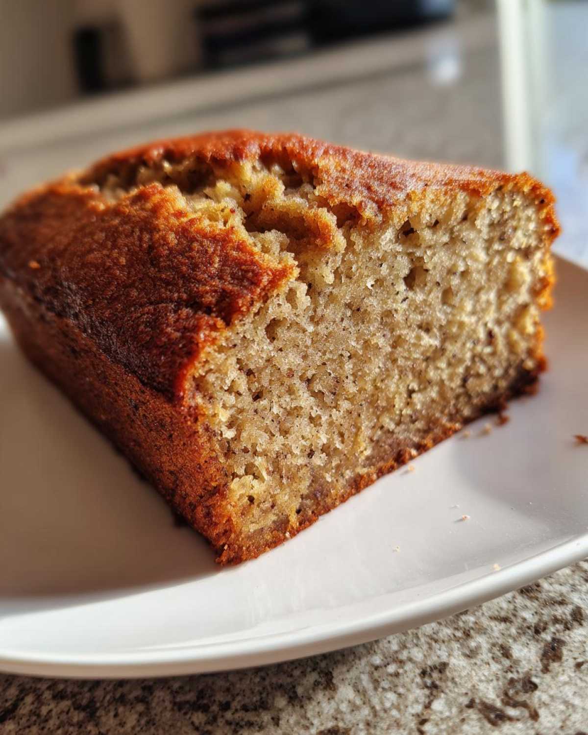 Close-up of a thick slice of moist sugar free banana bread with a golden brown crust, served on a white plate.